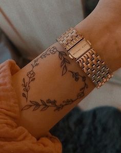 a woman's arm with tattoos on it and a gold bracelet that is attached to her wrist