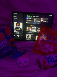 an open laptop computer sitting on top of a bed next to various snacks and candy