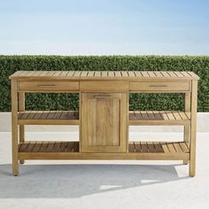 a wooden table sitting on top of a white floor next to a hedge covered wall