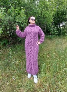 a woman standing in the grass wearing a purple knitted sweater and white socks with her hands up