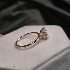 a gold ring with a pear shaped diamond on it sitting on a white display box