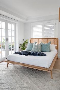 a bed with white sheets and blue pillows in a room next to sliding glass doors