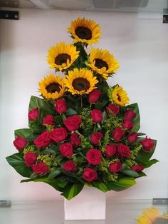 a bouquet of sunflowers and roses in a white vase with greenery on top