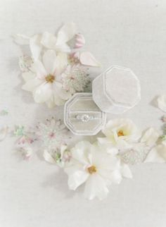 an open ring box surrounded by flowers on a white tablecloth with pink and white petals