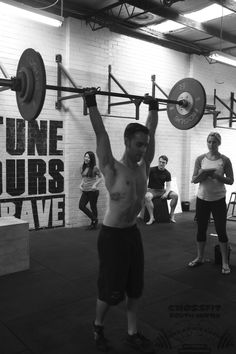 a man lifting a barbell in a crossfit gym with other people watching