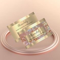 two gold foiled business cards sitting on top of a metal cable with a pink background