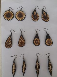 nine pairs of wooden earrings are displayed on a white sheet with black and gold designs