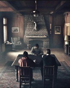 three people sitting at a table in front of a fireplace