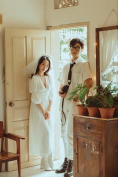 two people standing in front of a door wearing white dresses and black ties, one is holding a camera