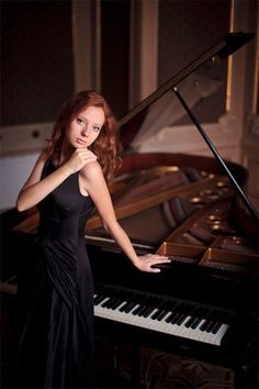 a woman in a black dress standing next to a piano