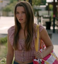 a young woman carrying a pink and white striped bag on her shoulder while walking down the street