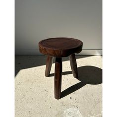 a small wooden stool sitting on top of a cement floor next to a white wall