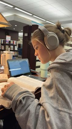 a woman sitting at a desk with headphones on and looking at an open book