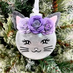 a cat ornament with purple flowers on it's head hanging from a christmas tree