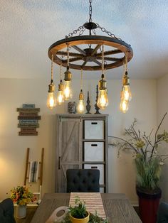 a dining room table with some lights hanging from it's centerpiece and potted plants on the side