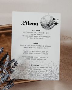 a menu card sitting on top of a wooden tray next to lavender flowers and a mirror