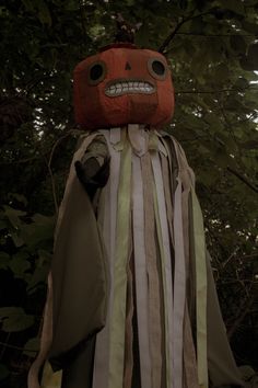 an odd looking costume is standing in front of some trees and leaves, with a creepy face on it's head