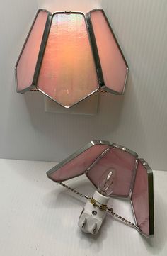 a light fixture with a pink shade on the side and a white wall behind it