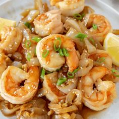 a white plate topped with cooked shrimp and onions next to a slice of lemon wedge