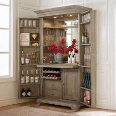 a bar with wine glasses, bottles and flowers on it in a room that has white walls