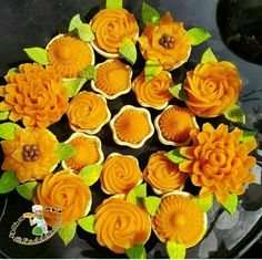 there are many cupcakes decorated with flowers on the cake platter and green leaves