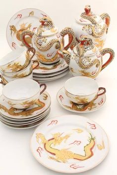 an assortment of porcelain dishes and cups with dragon designs on the sides, all decorated in gold