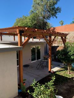 an outdoor patio with table and chairs under a wooden pergoline structure in the back yard