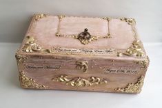 an antique pink and gold box with writing on the lid sits on a white surface