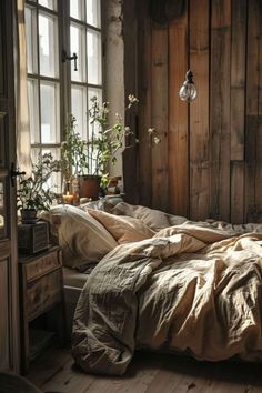 an unmade bed sitting next to a window in a room with wooden walls and flooring