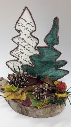 a decorative christmas tree made out of wood and paper with writing on the top, surrounded by autumn leaves