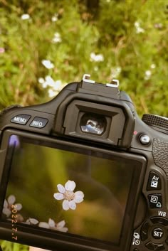 a camera with a flower on the screen is shown in front of some trees and bushes