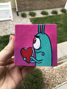 a hand holding up a piece of art that looks like a blue bunny with a heart