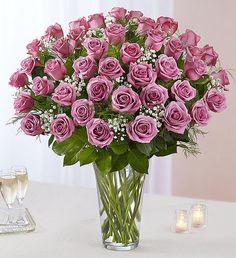 a vase filled with pink roses sitting on top of a table next to two candles