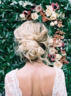 the back of a woman's head, with flowers in the background and greenery behind her