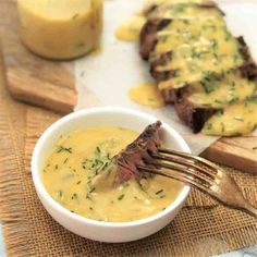 a fork in a bowl filled with soup next to some meat on a cutting board