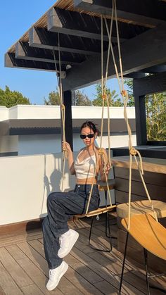 a woman is sitting on a swing with her legs crossed and sunglasses on, while she holds onto the rope