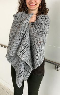 a woman wearing a gray knitted shawl standing in front of a white wall