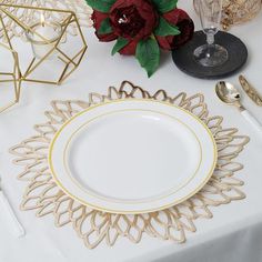 a white table topped with plates and silverware next to a vase filled with red flowers