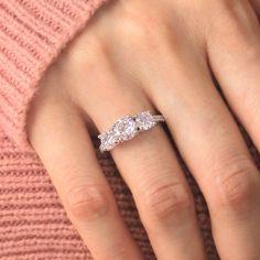 a woman's hand with three diamond rings on it and a pink sweater in the background