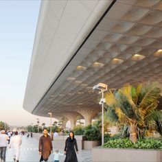 two people walking in front of a building with palm trees on both sides and an awning above them