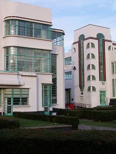 two white buildings with green windows and bushes in front of them on a sunny day