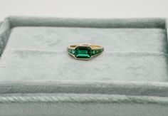 At the centerpiece of this lab grown Zambian emerald ring is a radiant 1.5 ct emerald, set east west to highlight its natural allure. Flanking it are calibre cut emeralds, each uniquely shaped to create a seamless gradient effect, making every ring truly one-of-a-kind. Set in luxurious 18K yellow gold, this ring exudes timeless charm. What makes it truly special? Calibre cut stones are individually shaped to fit precisely into the design, resulting in a mesmerizing display of color and brillianc Timeless Emerald Ring With Radiant Cut, Heirloom Emerald Ring Baguette Cut, Heirloom Baguette Cut Emerald Ring, Heirloom Style Baguette Cut Emerald Ring, Timeless Baguette Cut Emerald Ring Gift, Heirloom Green Baguette Cut Emerald Ring, Timeless Gift Baguette Cut Emerald Ring, Timeless Asscher Cut Green Emerald Ring, Timeless Baguette Cut Green Emerald Ring