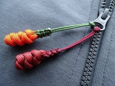 an orange and red knot is attached to the zipper of a gray jacket with a metal hook