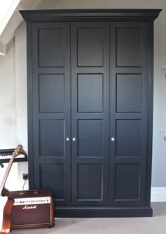 a black closet with an old fashioned guitar and amp in it's corner, next to a brown suitcase