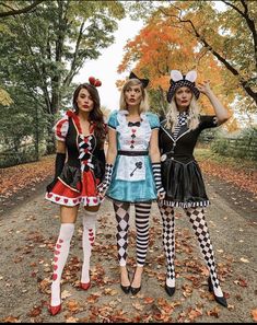 three women dressed in costumes posing for the camera on a dirt road surrounded by leaves