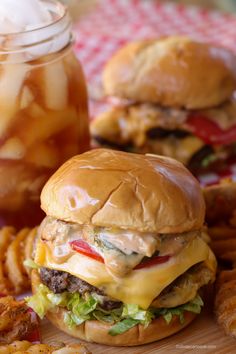 two hamburgers and french fries on a cutting board next to a jar of pickles