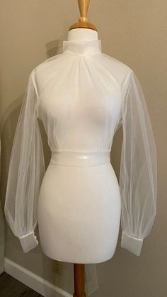 "Tulle wedding dress topper Mock turtle neckline with covered button closure at back neck Open 'V' back with long ties at back waist Bishop sleeves with cuffs/covered buttons **Made to order** Available up to 40\" bust Choose off-white or pale ivory - or ask for a specific color! Rush orders available - please ask about pricing & timing!" Elegant High Neck Tops With Mesh Sleeves, Elegant Tops With Sheer Sleeves And High Neck, High Neck Fitted Party Blouse, Fitted High Neck Blouse For Party, High Neck Fitted Blouse For Party, Elegant Sheer Tops For Wedding, Formal High Neck Fitted Blouse, Elegant High Neck Fitted Blouse, Elegant Fitted Tops For Weddings