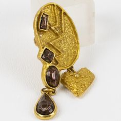 This stunning Christian Lacroix Paris signed pin brooch features a modernist shape in gilt metal all carved and textured topped with enameled bronze cabochons and complimented with a heart-dangling charm. A security closing clasp and hook are present at the back to use the brooch as a pendant. The brooch is signed at the back with the "Christian Lacroix - CL - Made in France" logo.  Measurements: 2.44 in high (6.2 cm) x 1 in wide (2.5 cm).  Please see the measurements noted above in the descript Unique Gold Pendant Brooches, Bronze Brooch Jewelry Gift, Unique Gold Brooches With Cabochon, Unique Gold Brooch With Cabochon, Ornate Bronze Brooches For Gifts, Yellow Gold Baroque Brooch For Gift, Modernist Gold Brooch Jewelry, Modernist Gold Brooches For Gifts, Christian Lacroix Jewelry Vintage