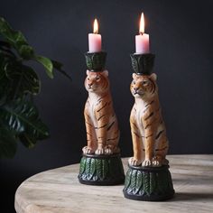 two candles are sitting on top of a table with a tiger figurine next to it