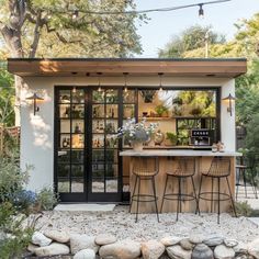 an outdoor bar with two stools in front of it and some plants on the counter